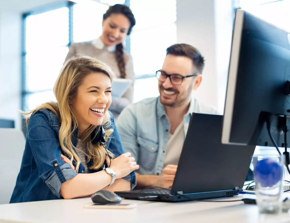 A man and woman smile together at a desk, engaged with a computer